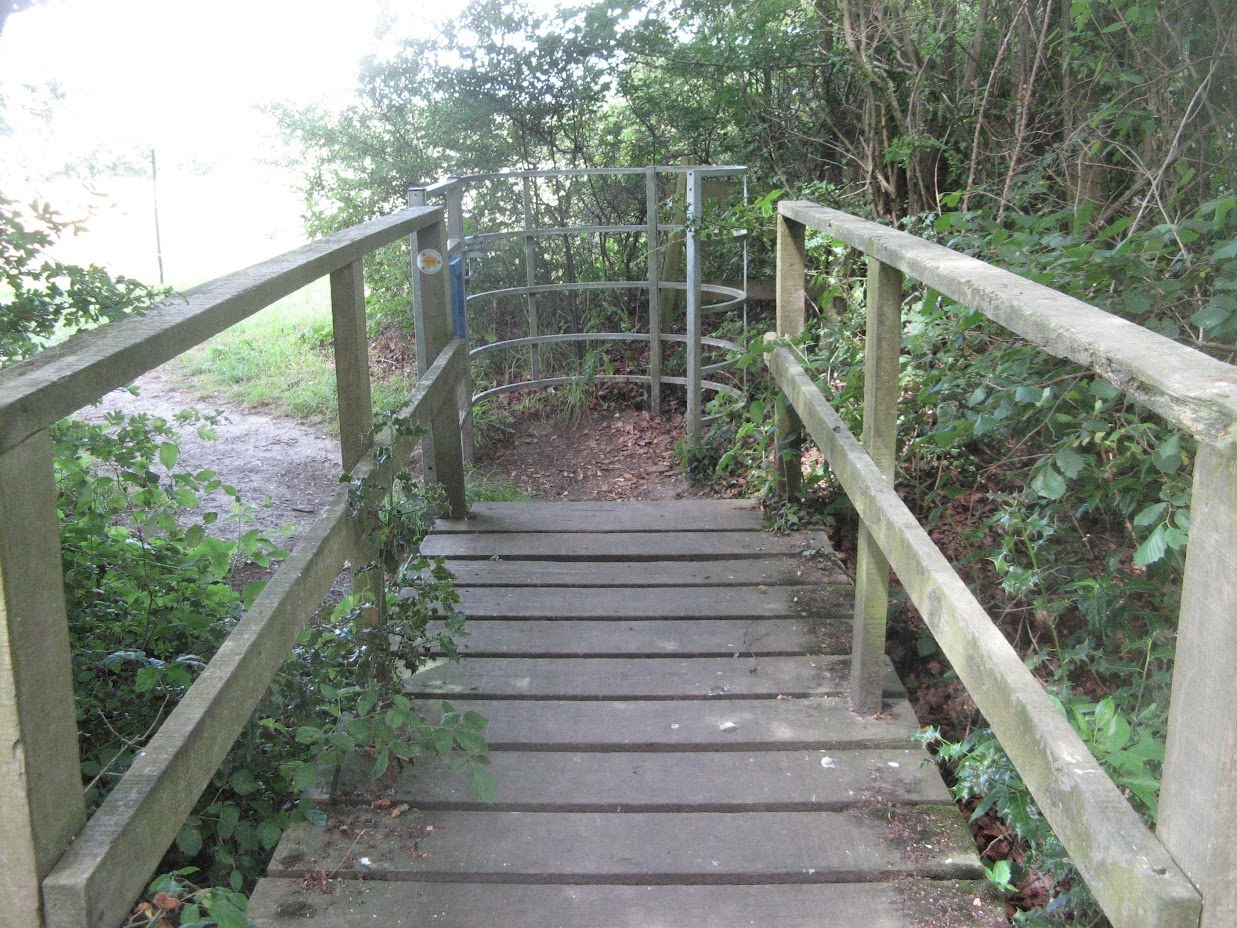Wooden footbridge leading to a metal kissing gate